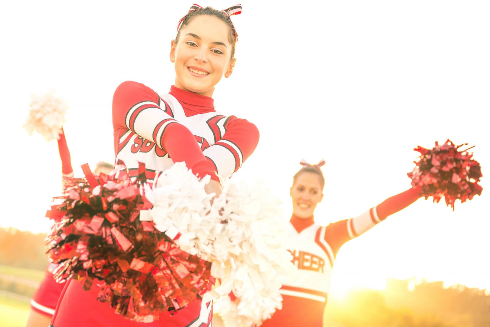 Tres cheerleaders, vestidas con trajes de equipo y pompones a juego, blanco y rojo