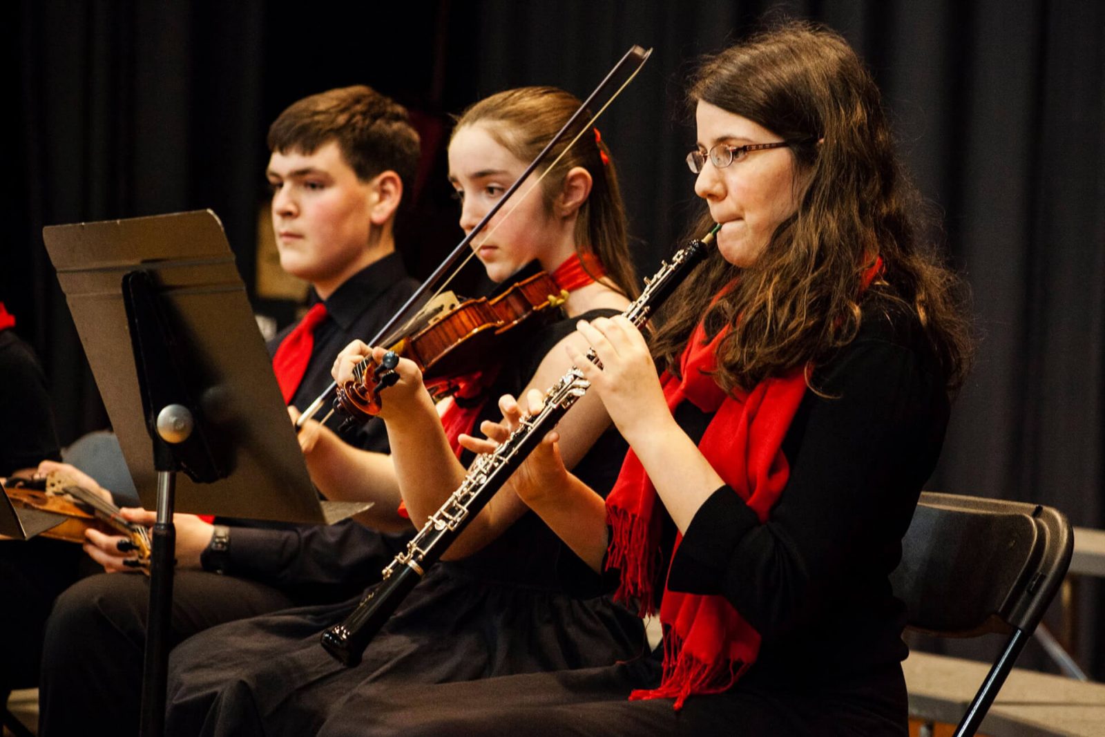 Dos chicas y un chico en un recital de música, tocan el clarinete y los violines