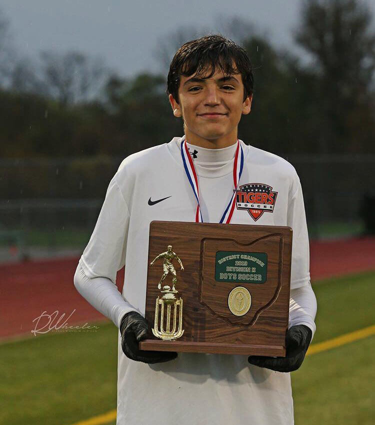 Estudiante, jugador de soccer de chicos, sujetando un premio bajo la lluvia.